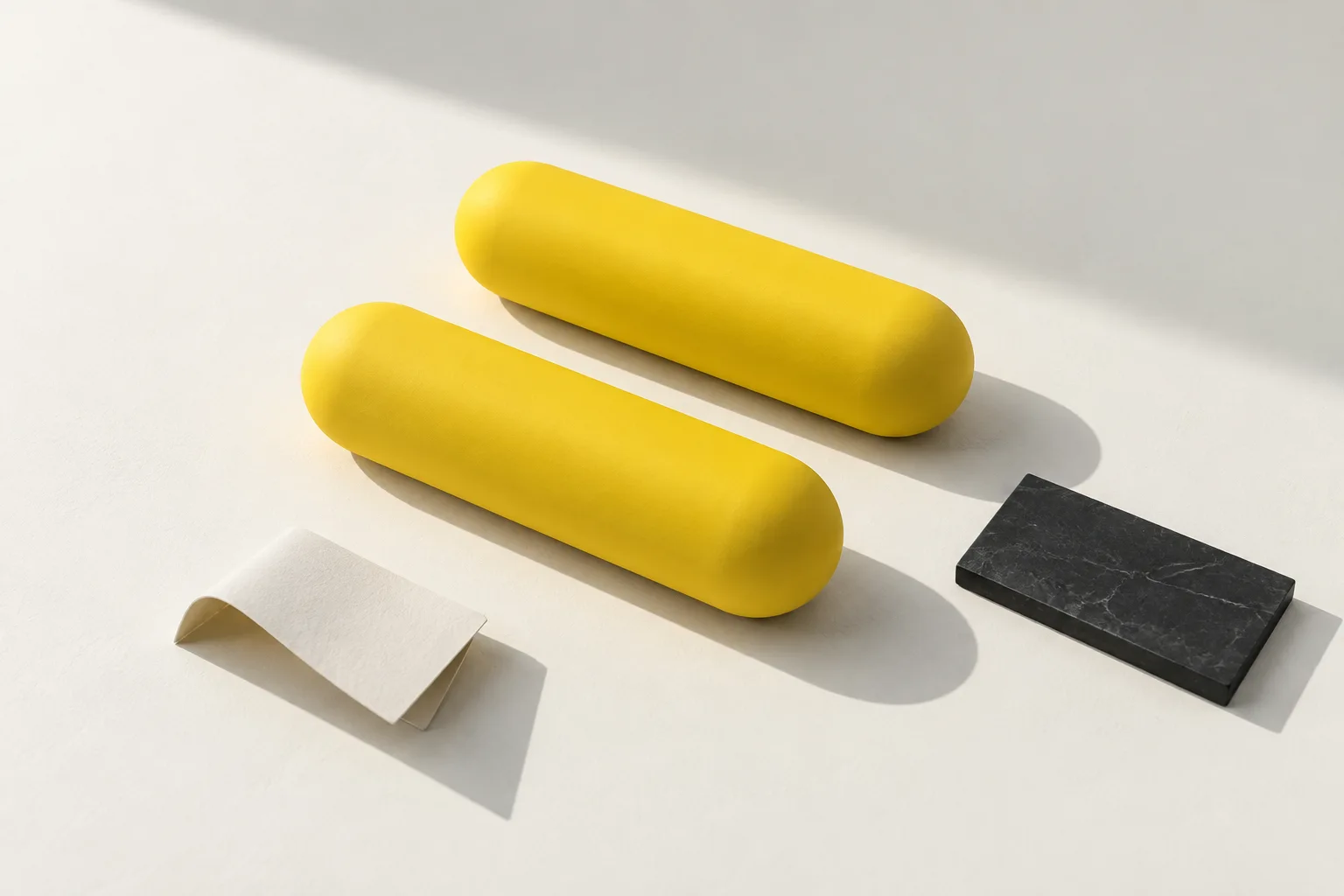 Two staggered yellow capsule forms with charcoal and paper elements in natural light